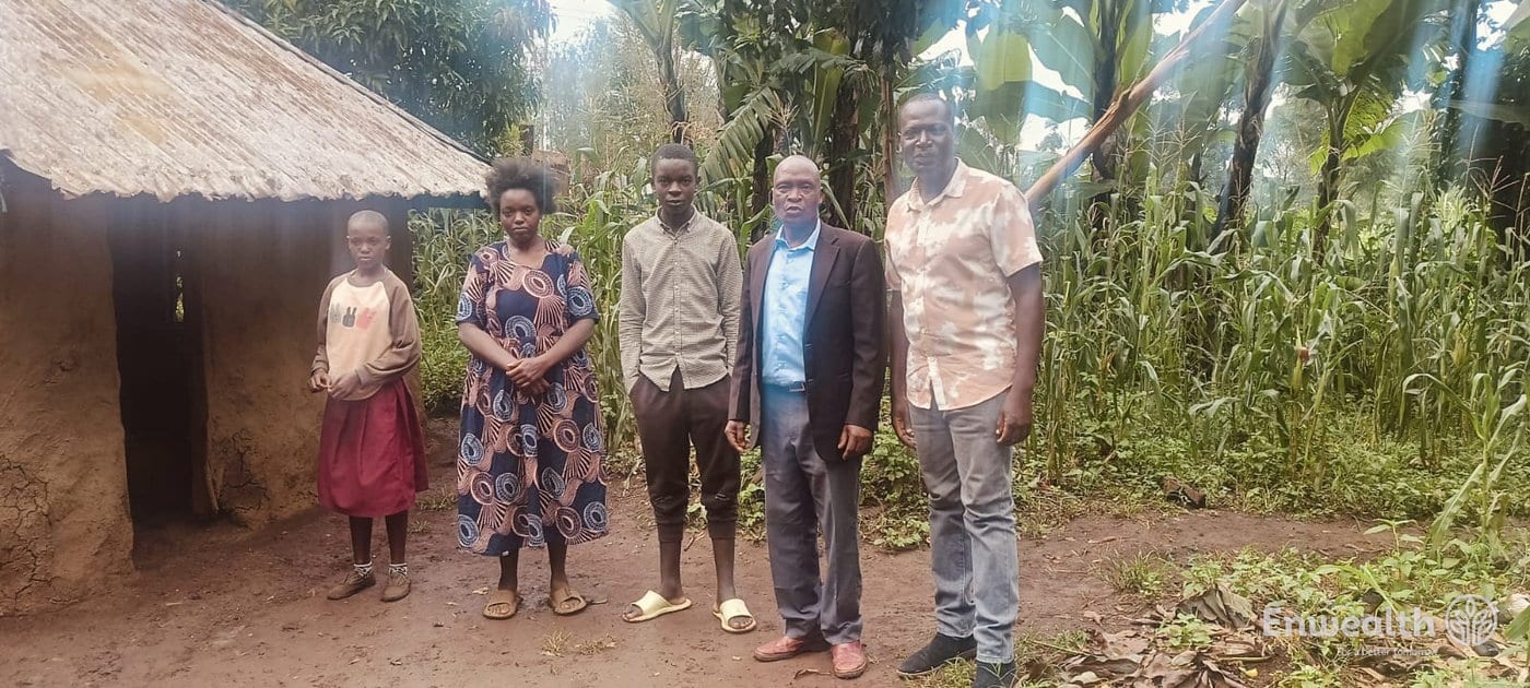 A woman and two children standing outside a mud-walled house with two Foundation staff.